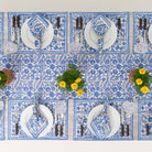 Set of blue and white patterned placemats with cutlery and plates on a white table.