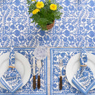 Table setting with blue floral tablecloth, white plates, and silverware on a white background.