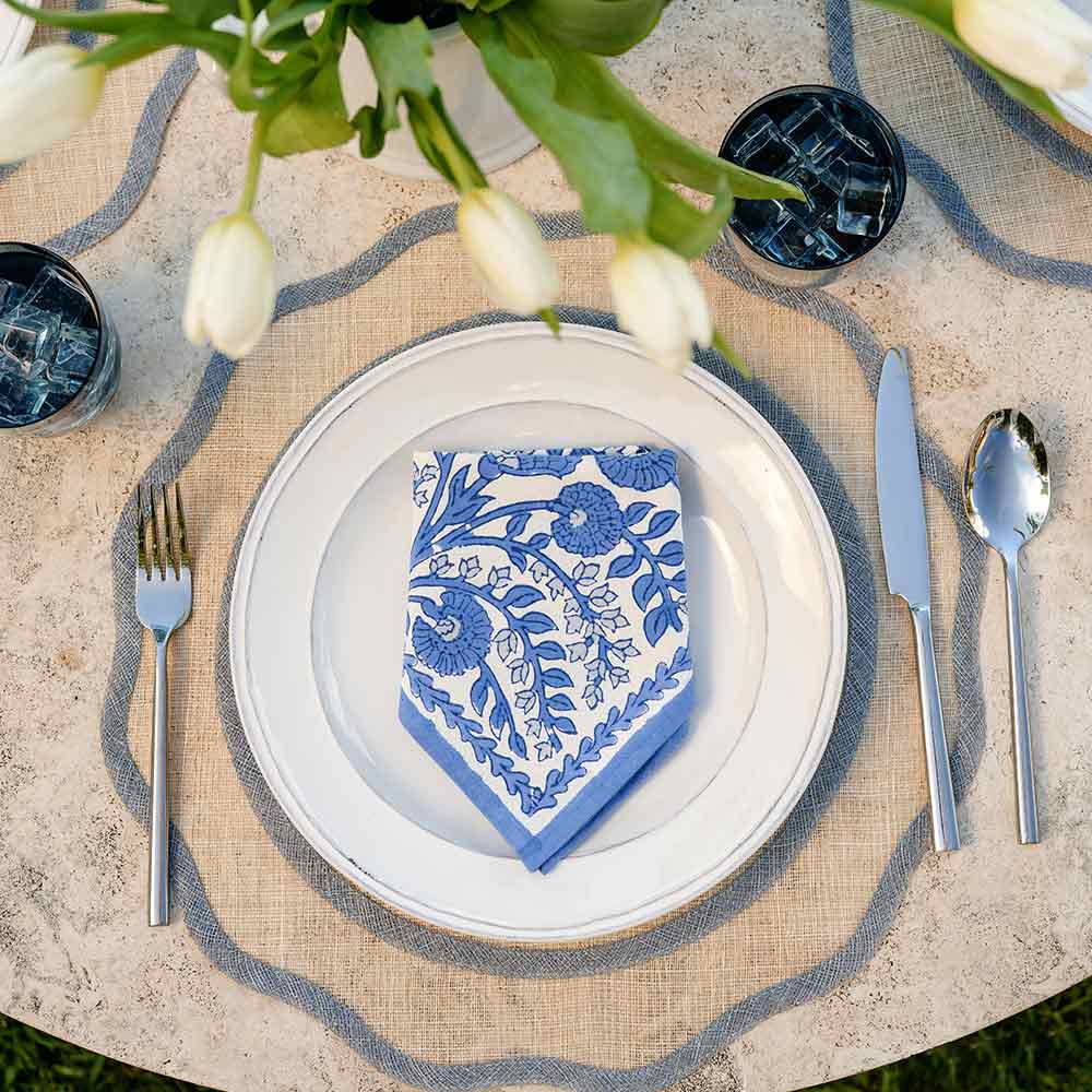Elegant table setting with a blue floral napkin on a white plate, silverware, and tulips.