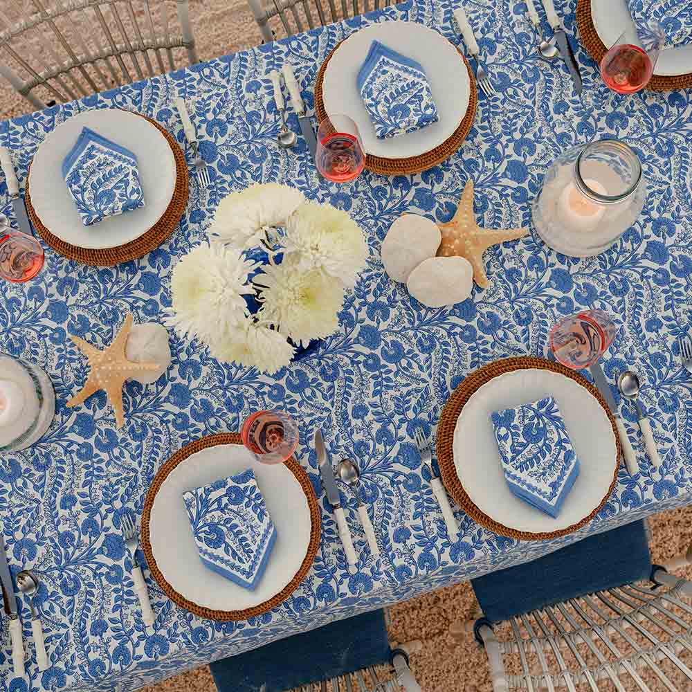 Table setting with blue and white floral tablecloth, plates, napkins, and decorative items.