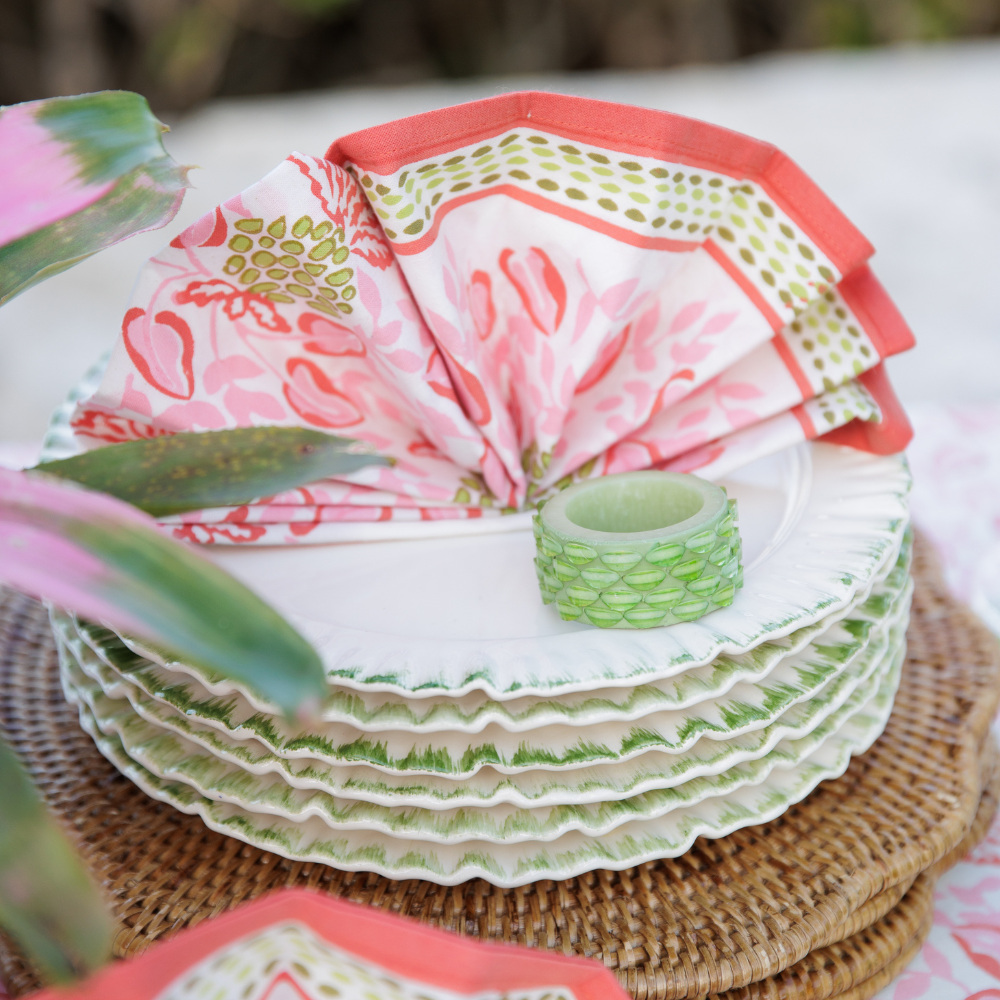 Stack of patterned plates with a floral napkin and green candle on a wicker tray.