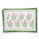 A set of four placemats with a floral pattern, featuring pink flowers and green leaves on a white background, placed on a white surface.