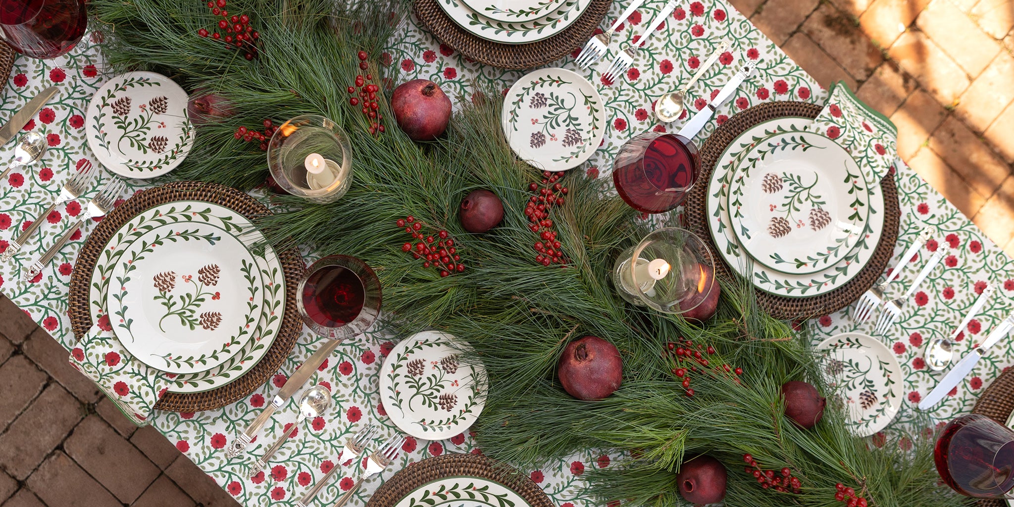Decorative table setting with plates, candles, and greenery on a patterned tablecloth.
