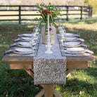 Dining table set with plates, glasses, and a floral centerpiece outdoors.
