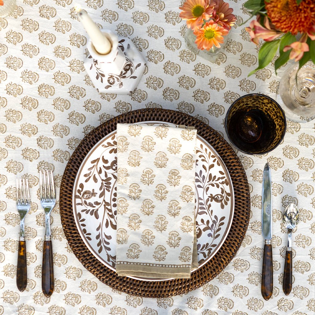 folded beige and white indian print napkin on a plate sitting on a tablecloth