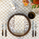 folded beige and white indian print napkin on a plate sitting on a tablecloth