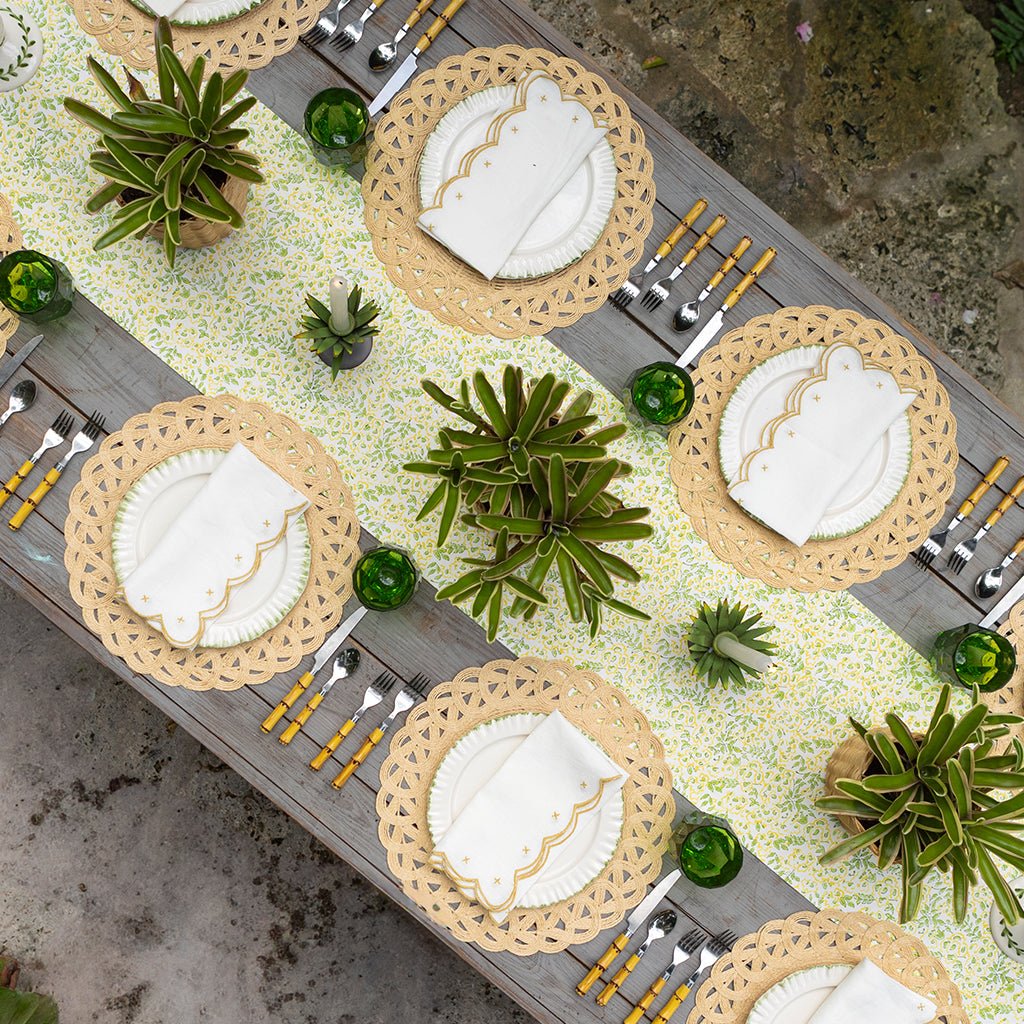 Decorative table setting with woven placemats, white napkins, and green centerpieces.