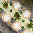 Decorative table setting with woven placemats, white napkins, and green centerpieces.