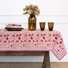 Table with a patterned tablecloth, vase with flowers, and glasses on a white wall background