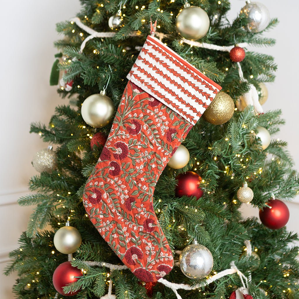 Decorative red Christmas stocking hanging on a Christmas tree with ornaments.