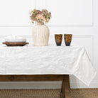 Table setting with a white tablecloth, vase with flowers, and decorative items on a wooden table.