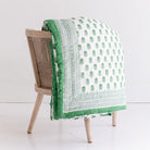 Green and white patterned quilt draped over a wooden chair on a white background