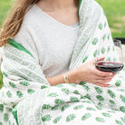 Person holding a glass of red wine wrapped in a green and white patterned shawl.
