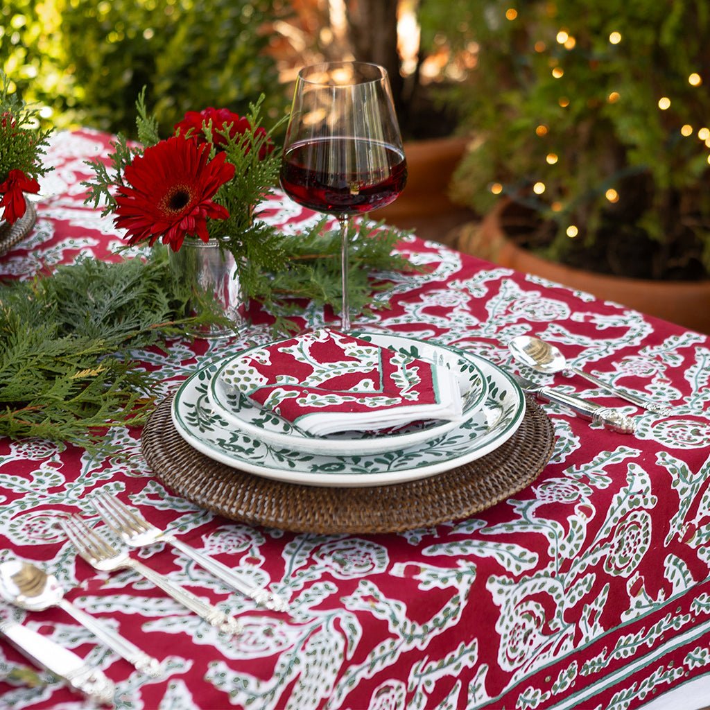 Elegant table setting with red and white patterned tablecloth, greenery, and wine glass.