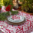 Elegant table setting with red and white patterned tablecloth, greenery, and wine glass.