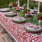 Decorative table setting with red and white patterned tablecloth, greenery, and wine glasses.