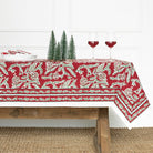 Tablecloth with reindeer design on a wooden table with wine glasses and Christmas trees.