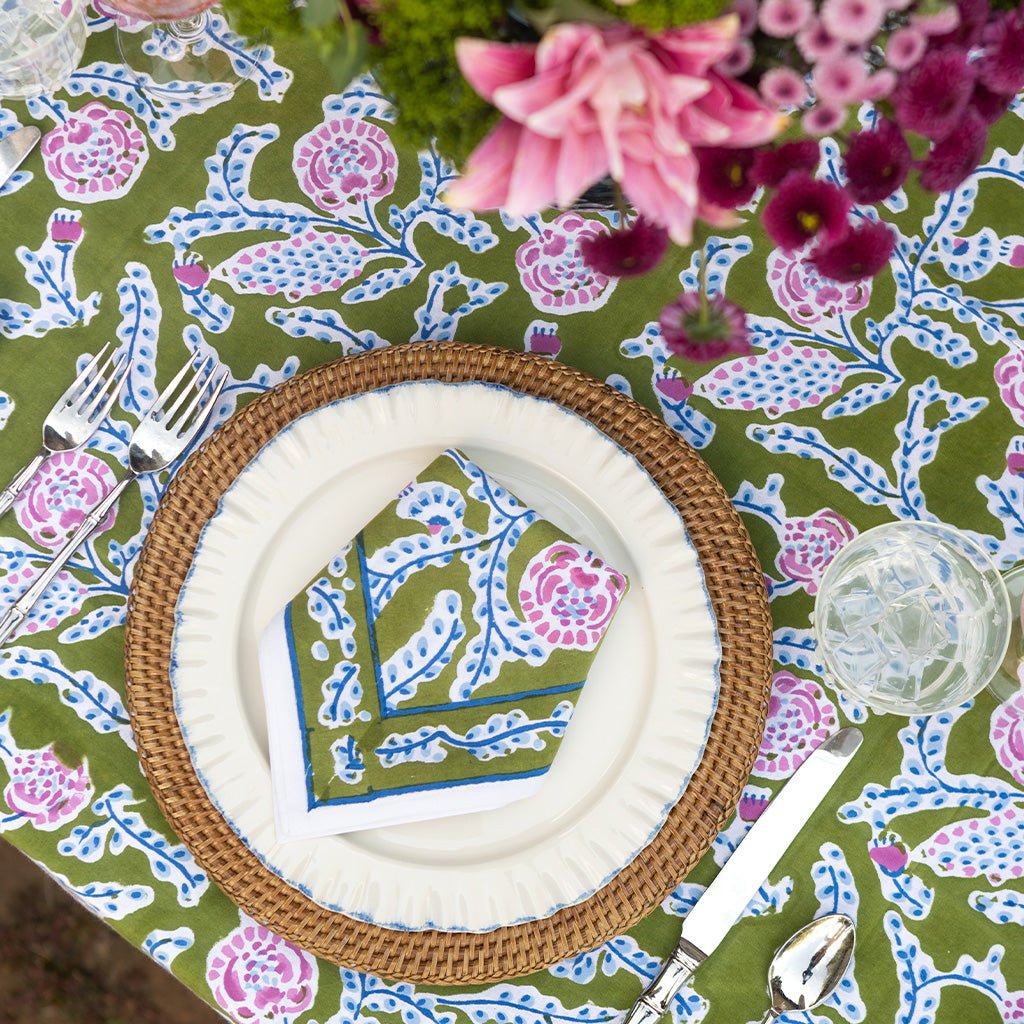 Green, blue, and purple patterned cloth napkin set on a ceramic plate and rattan charger. 