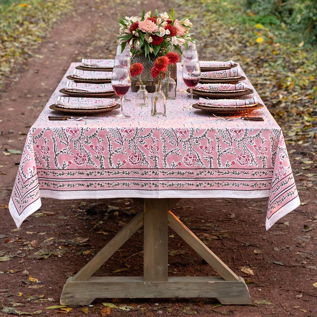 Dining table set with a pink and white patterned tablecloth outdoors.