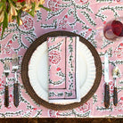 Table setting with floral tablecloth, plates, cutlery, and napkin on a decorative pink and green tablecloth.
