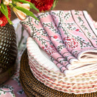 Stack of folded fabric with floral pattern on a woven surface with flowers in the background
