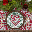 Decorative Christmas table setting with a red and green patterned tablecloth, white plate with red heart design, and silverware.