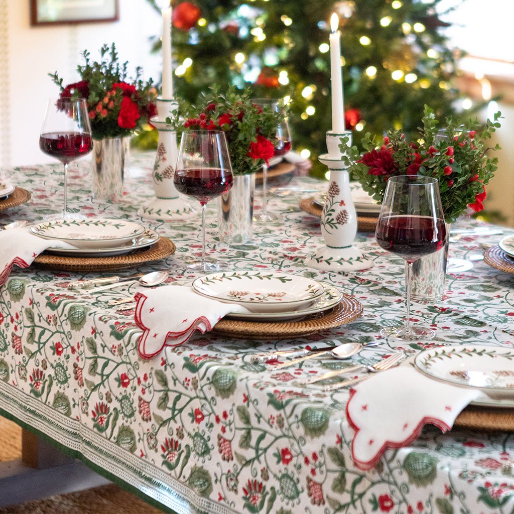 Decorative Christmas table setting with floral centerpieces, wine glasses, and a tree in the background.