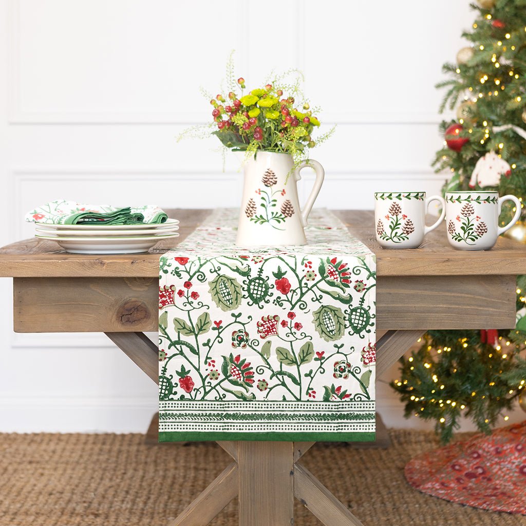Decorative table setting with floral-patterned tablecloth, pitcher, and mugs on a wooden table.