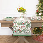 Decorative table setting with floral-patterned tablecloth, pitcher, and mugs on a wooden table.