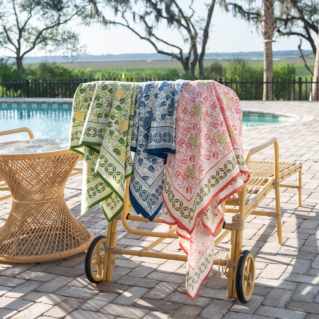 Three patterned towels draped over a cart by a poolside.