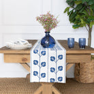 Table setting with a blue and white table runner, blue vase, and glasses on a wooden table.