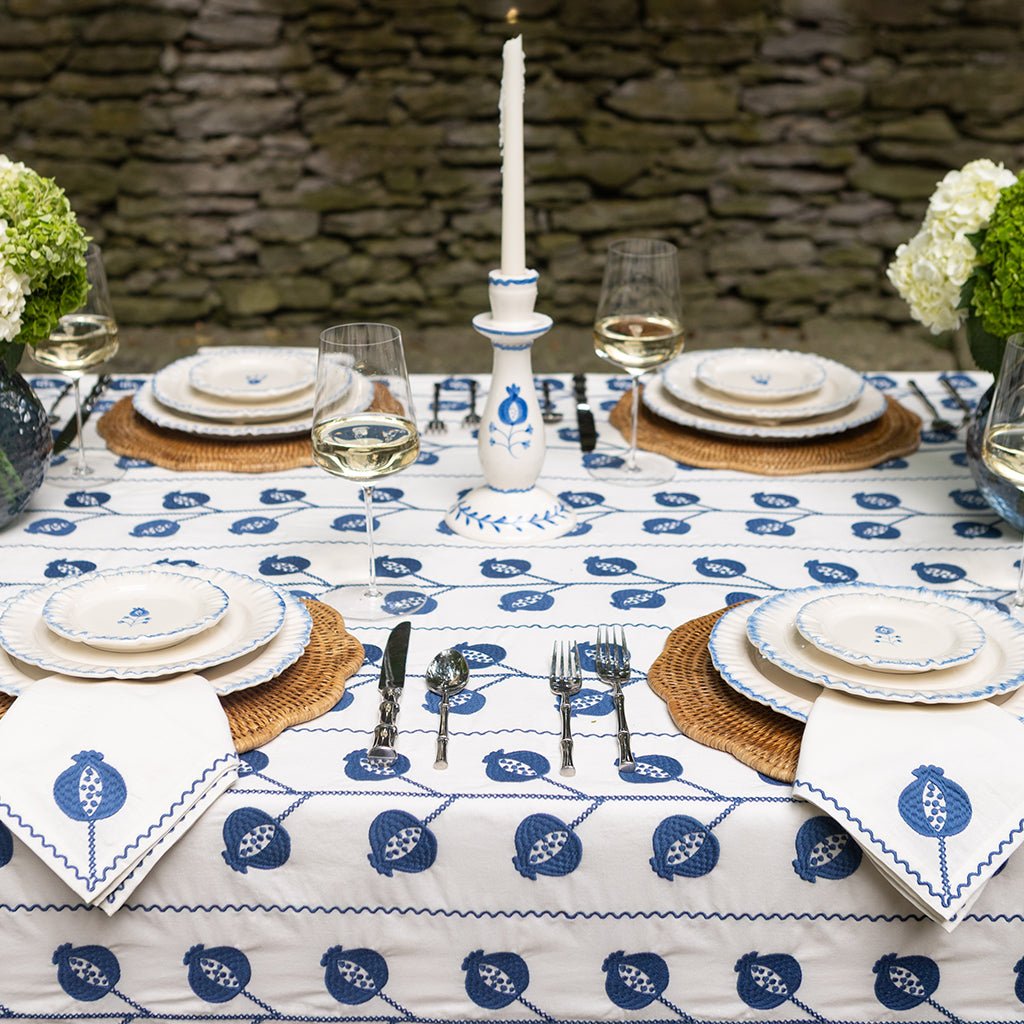 Dining table set with blue and white patterned tablecloth, plates, cutlery, and candles.