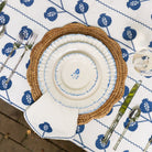 Table setting with woven placemat, white plates, and blue patterned tablecloth.