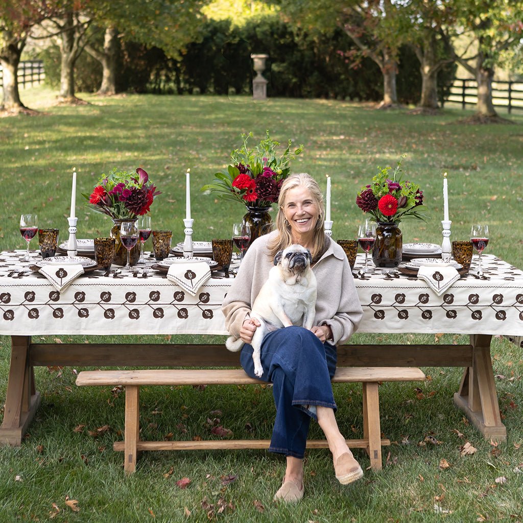 Woman sitting on a bench with a dog, both in front of an outdoor dining table set for a meal.