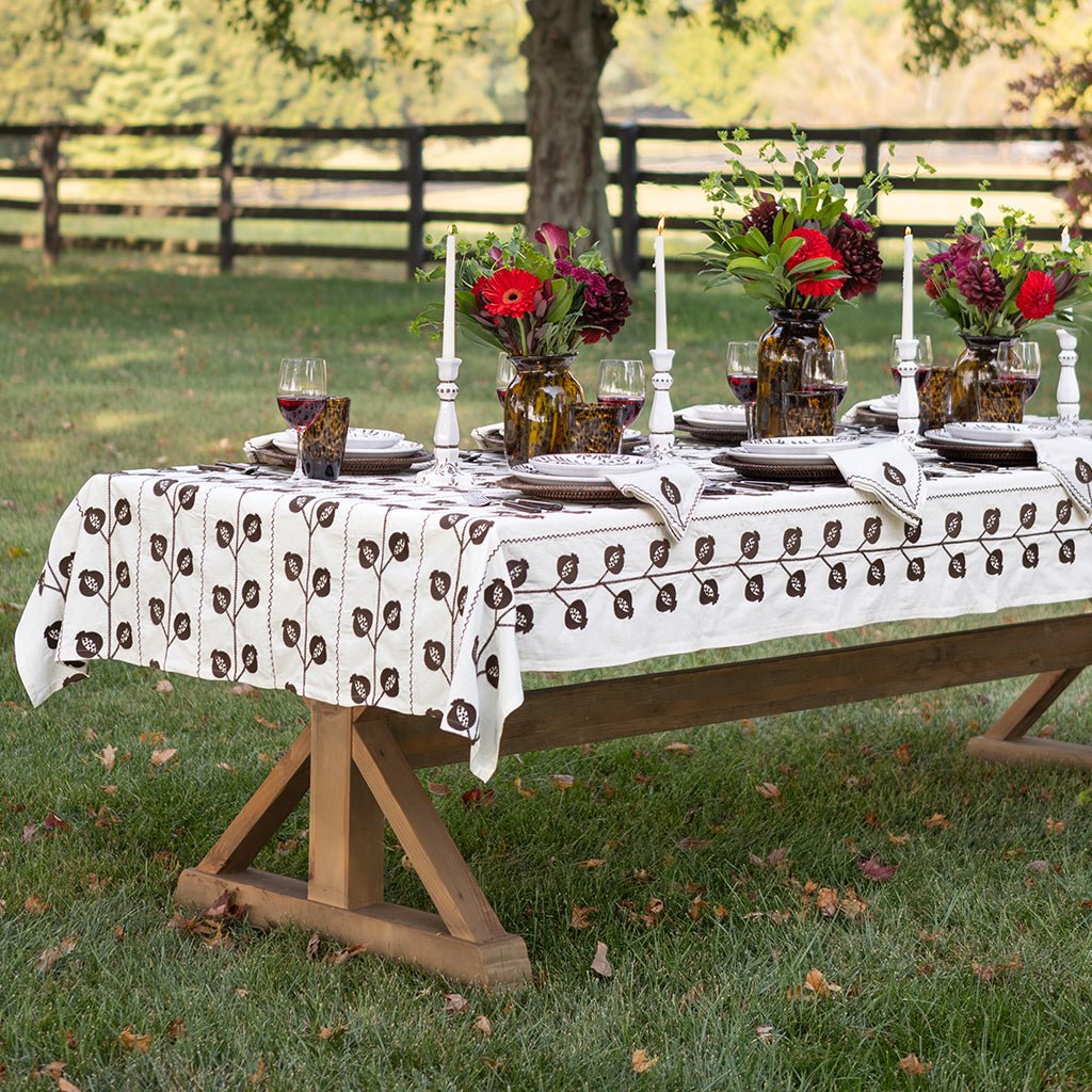 Dining table set outdoors with floral centerpieces and a patterned tablecloth.