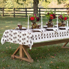 Dining table set outdoors with floral centerpieces and a patterned tablecloth.