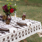 Dining table set with a floral centerpiece, glasses, and cutlery on a patterned tablecloth outdoors.