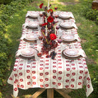 Dining table set with a floral tablecloth, plates, glasses, and flowers outdoors.