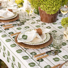Dining table setting with green and white patterned tablecloth, wicker plates, and cutlery.