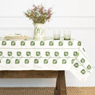 Tablecloth with green leaf pattern on a wooden table with a vase of flowers and glasses.