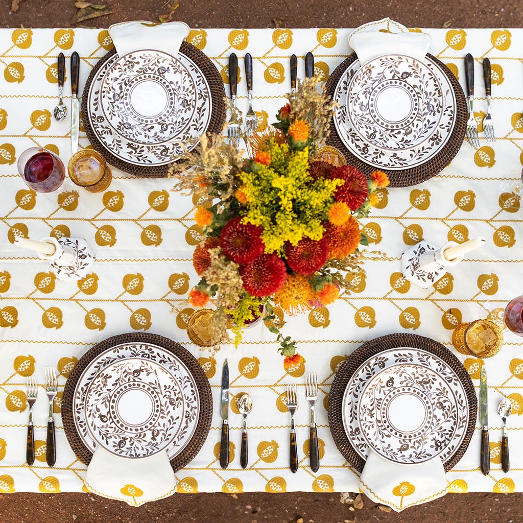Elegant table setting with decorative plates, cutlery, and a floral centerpiece on a patterned tablecloth.