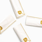 White napkins with gold trim and embroidered designs on a white background