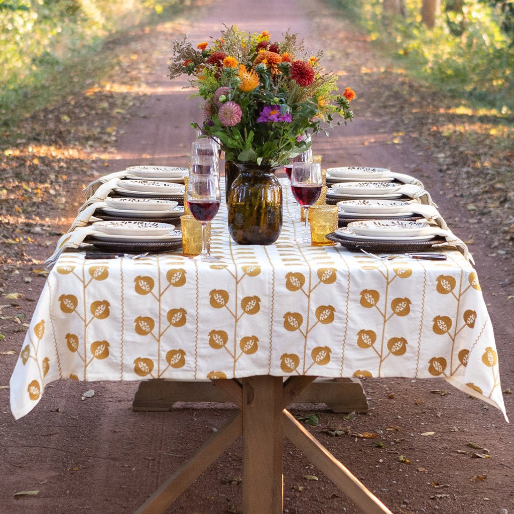 Dining table set with a floral tablecloth, plates, glasses, and a vase of flowers outdoors.