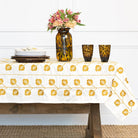 Table setting with a white tablecloth featuring yellow floral patterns, a vase with flowers, and leopard print glasses.