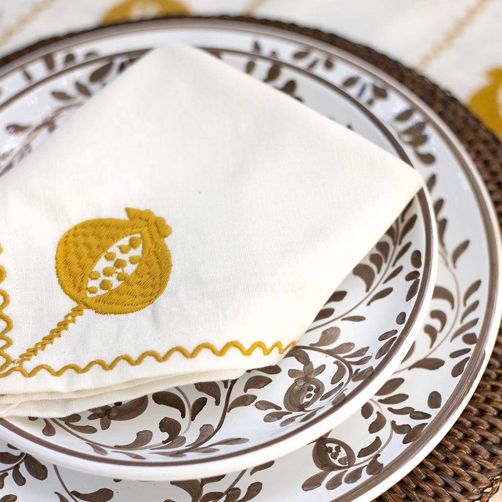 White napkin with ochre embroidery on a patterned plate