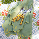 Set of green napkins with embroidered designs on a floral tablecloth.