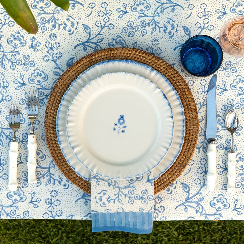 Dining table setting with white plates, blue floral patterns, and silverware on a decorative tablecloth.