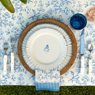 Dining table setting with white plates, blue floral patterns, and silverware on a decorative tablecloth.