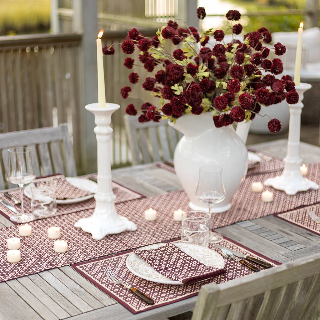 Elegant outdoor dining table setting with red flowers, candles, and white candlesticks.