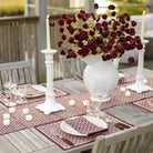 Elegant outdoor dining table setting with red flowers, candles, and white candlesticks.